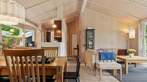 Ein geräumiges Zimmer mit Holzböden und -decken, einer Essecke mit Tisch und Stühlen, einer Couch und einem Schrank.