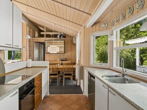 A modern kitchen with wooden cabinets, a built-in oven, a sink, and a dining area with a table and chairs.