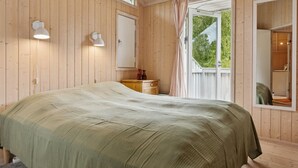 Ein Zimmer mit Holzboden, einem Bett, einem Nachttisch, einem Spiegel und einem Fenster mit Vorhängen.