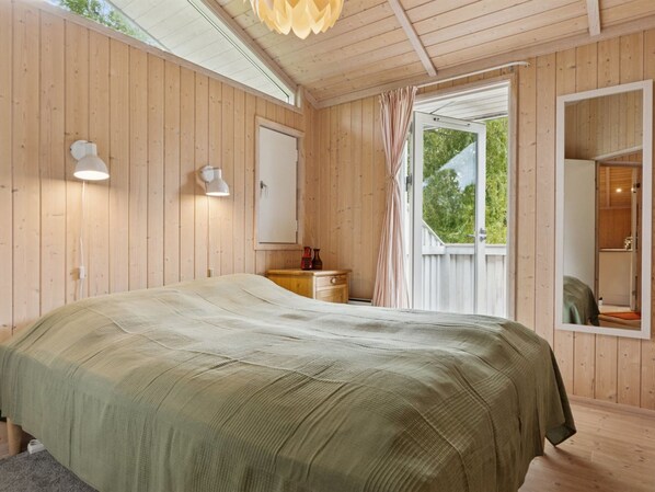 Une pièce en bois avec un lit, une table de chevet, un miroir et une fenêtre avec des rideaux.