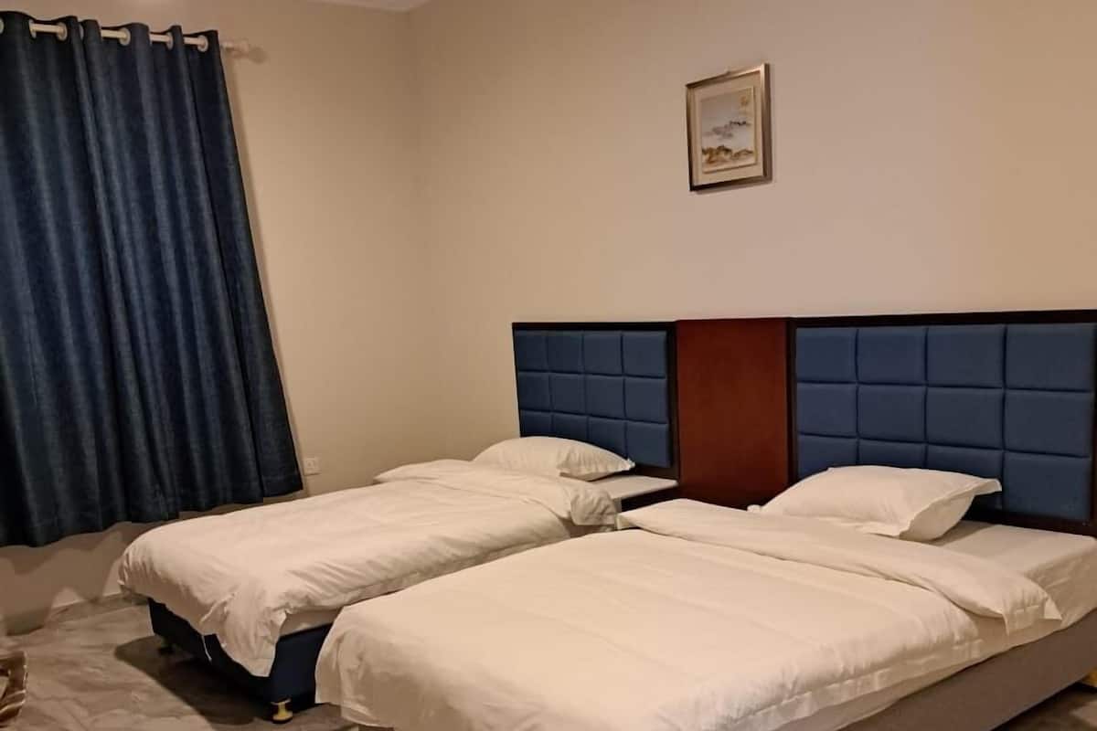 A hotel room with two beds, a blue headboard, a framed picture on the wall, and a blue curtain.