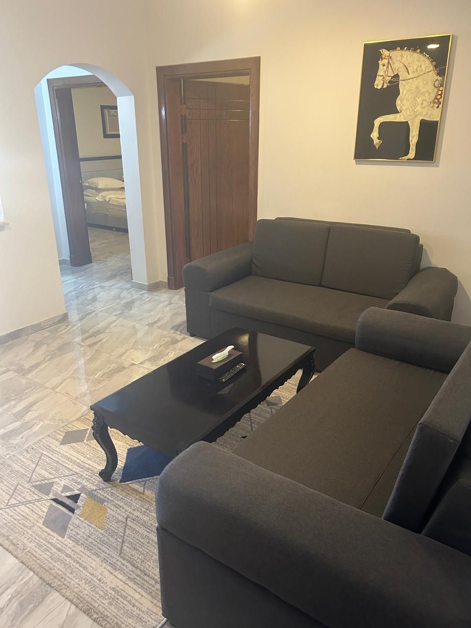 Una sala de estar con un sofá gris, una mesa de centro negra y una obra de arte de un caballo enmarcada en la pared.