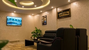 Ein stilvoller Lounge-Bereich mit einem schwarzen Ledersofa, einem Flachbildfernseher, einem gerahmten Bild und einem Blumentopf.