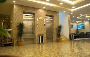 A lobby with marble flooring, two elevators, potted plants, a reception desk, and a television screen.