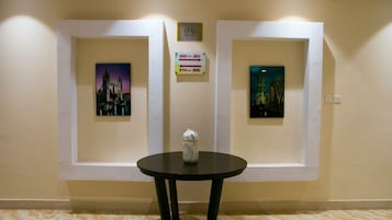 A hallway with two framed pictures on the walls, a small table with a vase, and directional signs above the door.