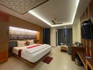 A modern hotel room with a large bed, a desk, a television, and a ceiling fan.