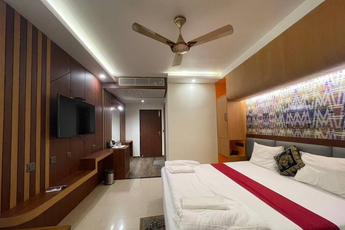 Une chambre d’hôtel équipée d’un lit, d’une télévision, d’un ventilateur de plafond et d’une tête de lit à motifs.