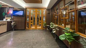 A reception area with a wooden reception desk, a television screen, and a set of glass doors. - ASHA PREMIUM (Kanthi)