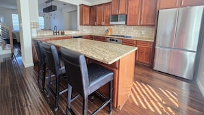 Una cucina moderna con mobili in legno, un piano di lavoro in granito, elettrodomestici in acciaio inossidabile e un'area bar con sgabelli.