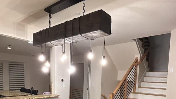 Un'area pranzo moderna con un tavolo e sedie in legno, un lampadario e una scala che conduce a un piano superiore.