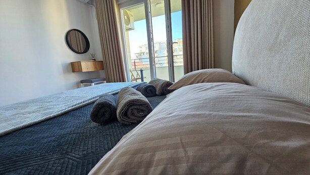 Habitación de hotel con cama, ventana con cortinas, mesita de noche y aire acondicionado instalado en la pared.