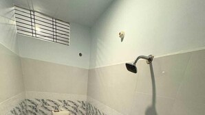 Une petite salle de bain carrelée, équipée de toilettes, d’une douche et d’un lavabo.