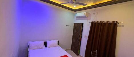 A hotel room with a bed, a ceiling fan, an air conditioning unit, a door, and a curtain.