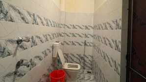 Une salle de bain avec des murs en marbre, des toilettes, une douche et un seau rouge.