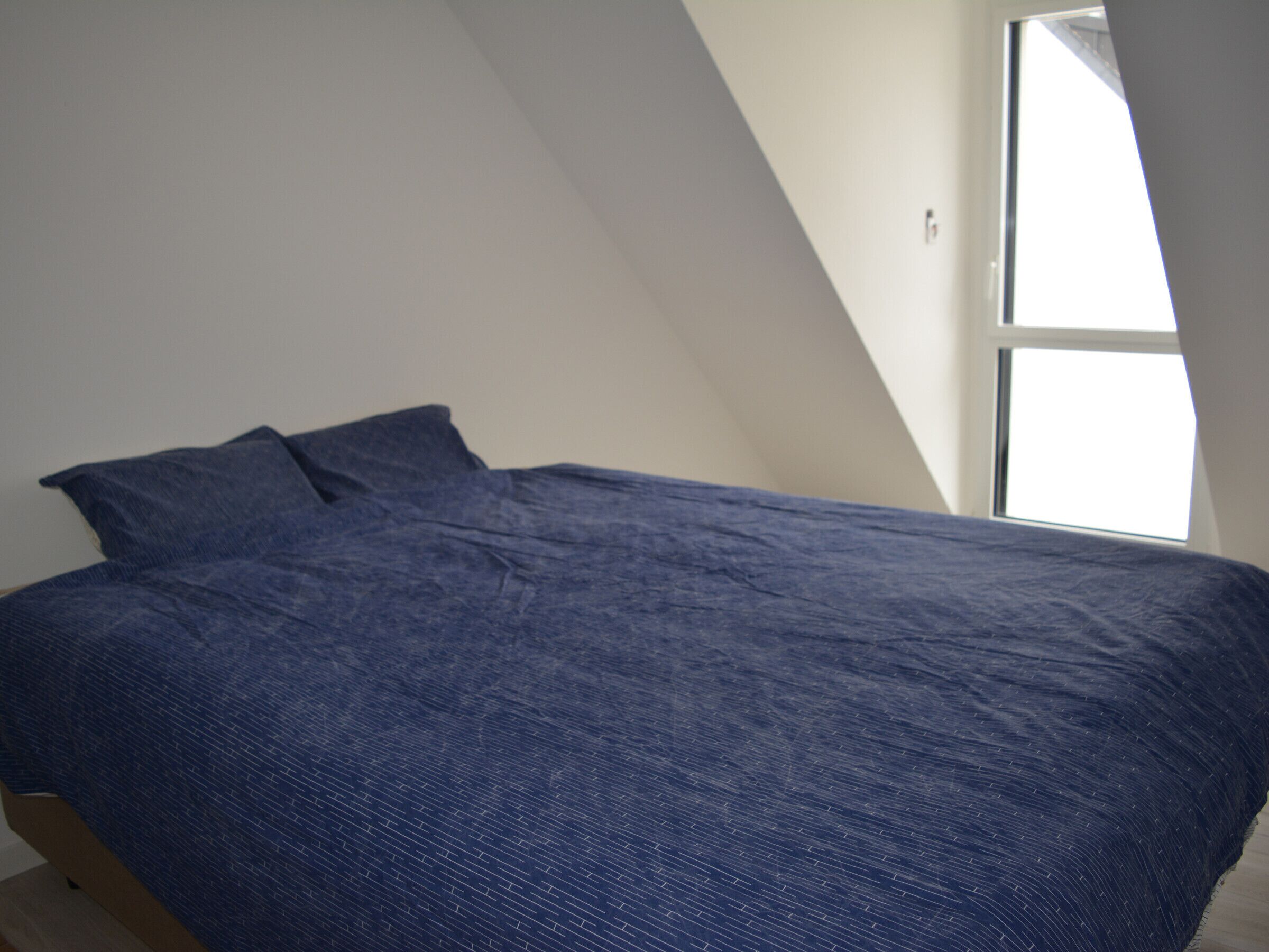 A bedroom with a bed, pillows, and a window.