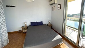 A bedroom with a bed, a hanging light fixture, a window with a view, and an air conditioning unit. - Apartment panoramic view, AC and parking - 4 guests (Argelès-sur-Mer)