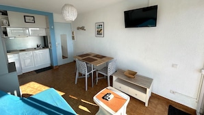 A compact living space with a kitchenette, a dining area, a TV mounted on the wall, and a small table with a chair. - Apartment panoramic view, AC and parking - 4 guests (Argelès-sur-Mer)