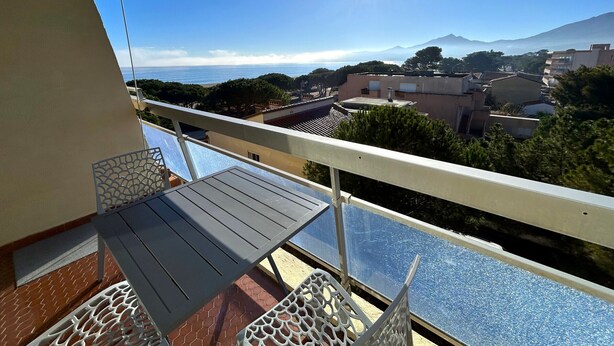A balcony with a table and chairs, overlooking a cityscape and a body of water. - Apartment panoramic view, AC and parking - 4 guests (Argelès-sur-Mer)