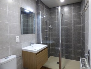 A modern bathroom with a glass shower enclosure, a white sink, and a wooden vanity.