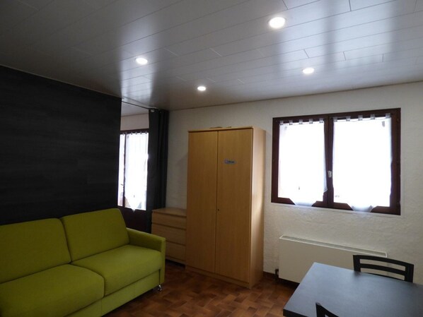 A room with a green sofa, a wooden wardrobe, a table, and a window with curtains.