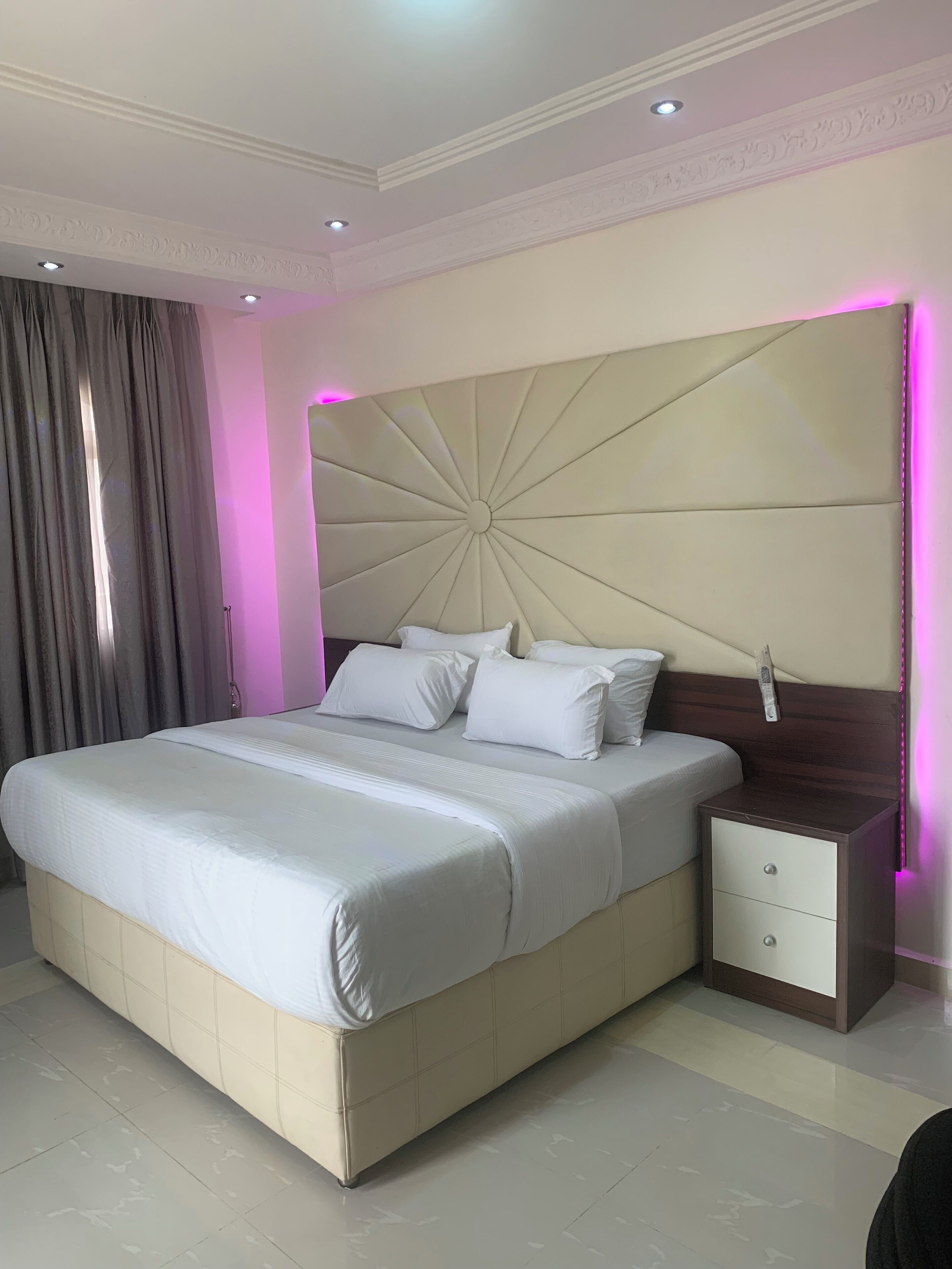 Un dormitorio con una cama grande, una mesita de noche con cajones, un cabecero decorativo y una ventana con cortinas.