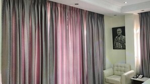 Una habitación de hotel con un ventanal grande, una silla, una cama y un cuadro en la pared.