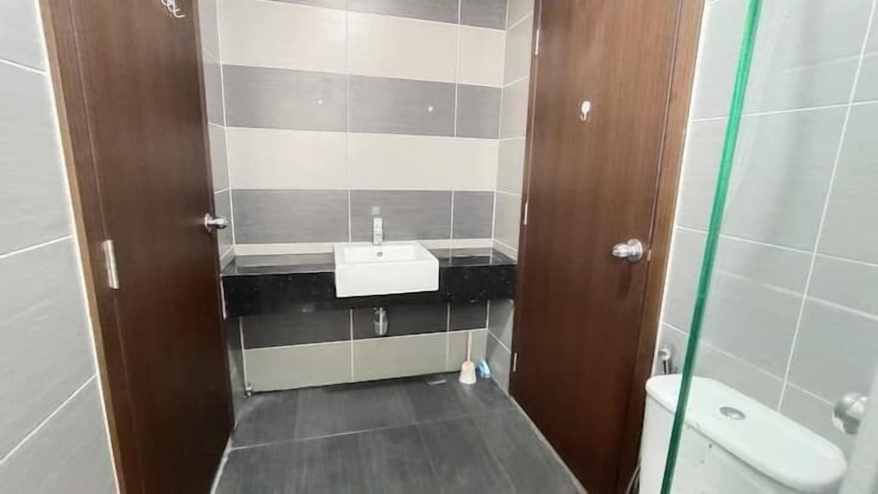 A small bathroom with a white sink, dark tiles, and a glass shower enclosure.