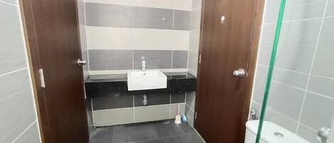 A small bathroom with a white sink, dark tiles, and a glass shower enclosure.