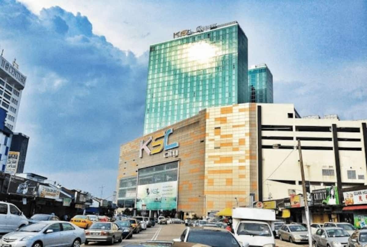 Un edificio de varios pisos con un llamativo letrero 'KSL', rodeado de automóviles estacionados y otros edificios.