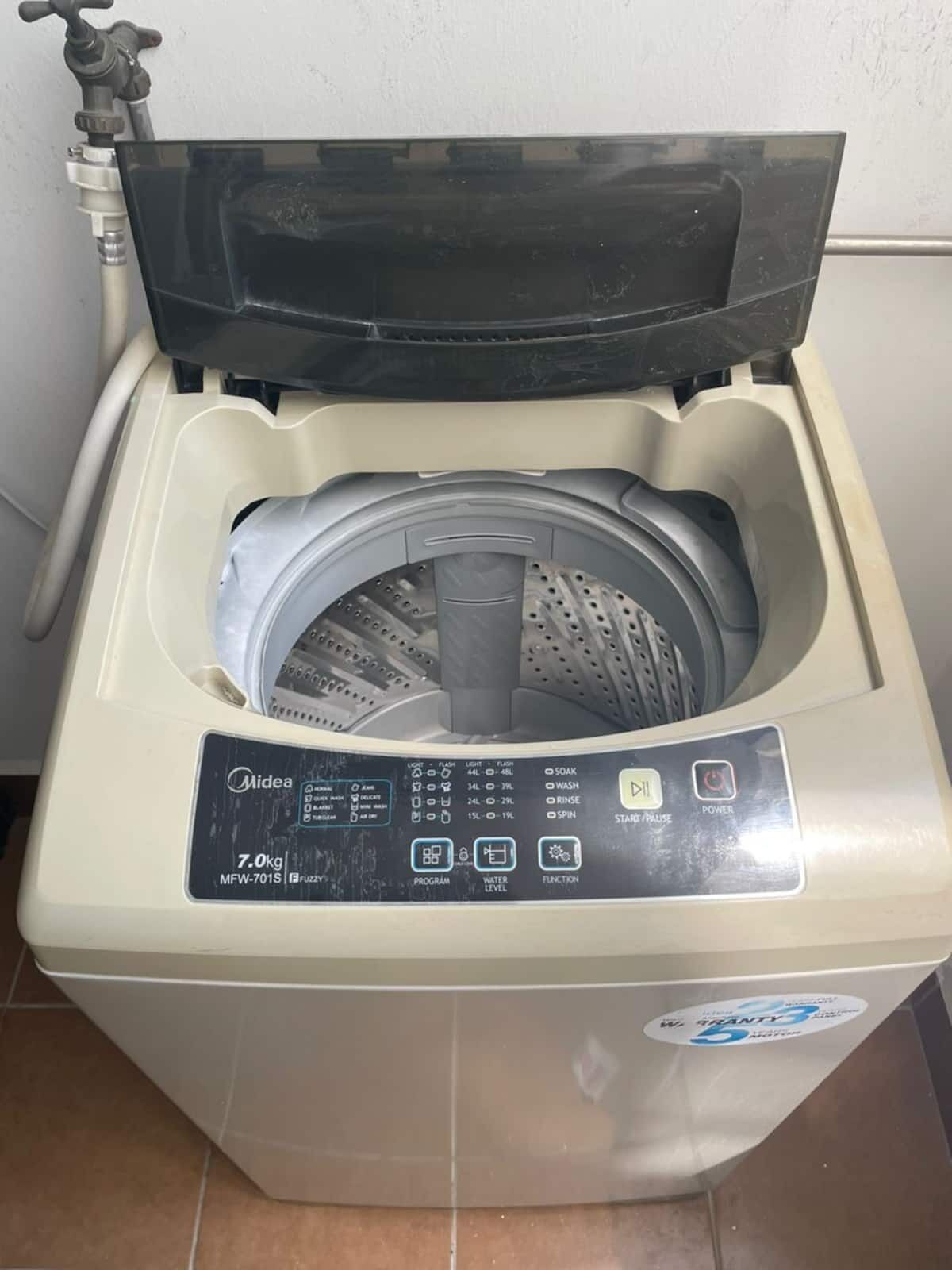 A front-loading washing machine with a control panel, a water inlet, and a drain hose.