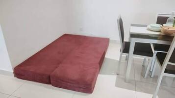 A room with a red mattress on the floor, a white table with chairs, and a small table with a bowl and a plant.