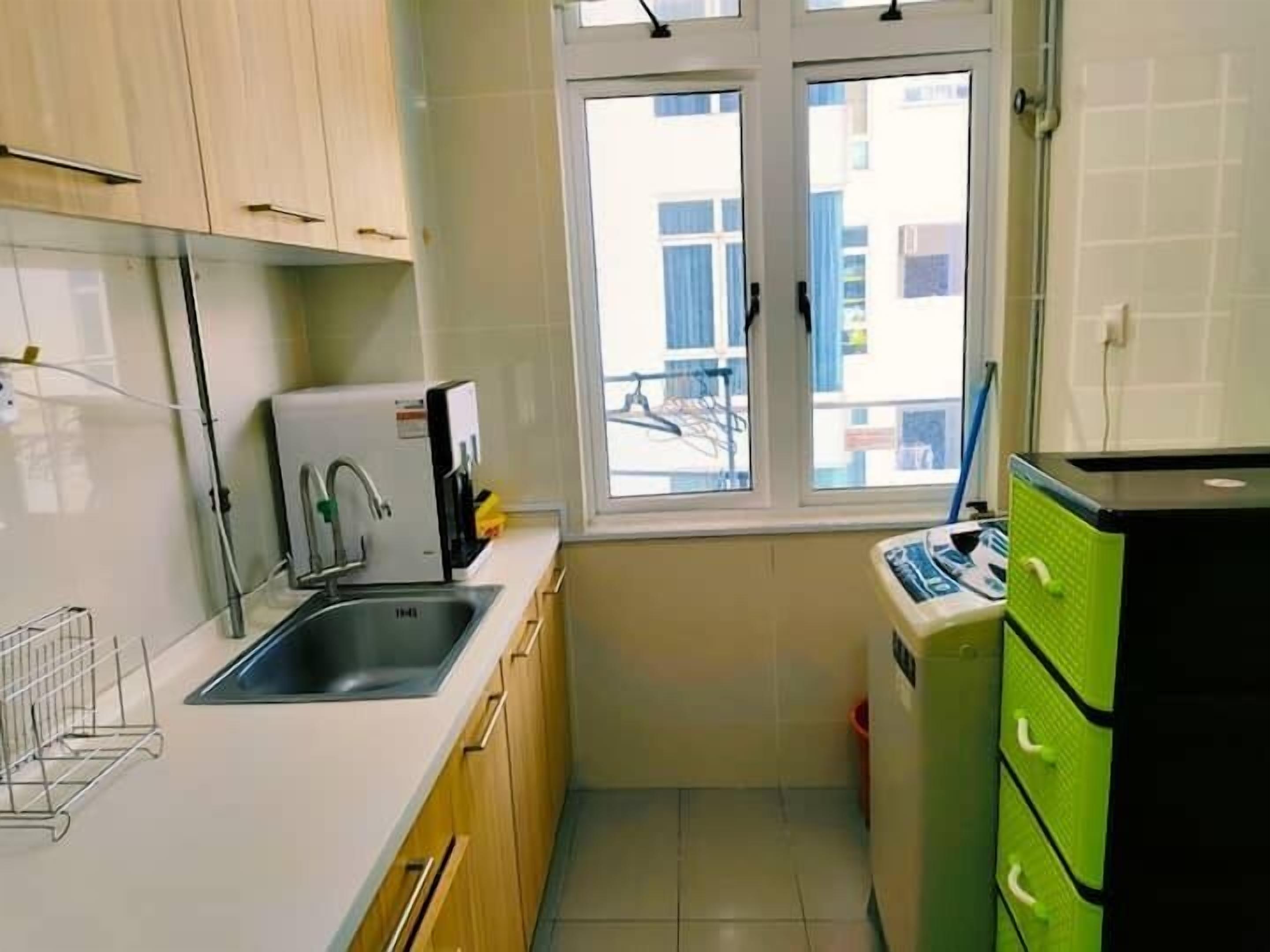 A compact kitchen with a sink, a coffee machine, and a green appliance, likely a food processor or blender, with a window above the sink.