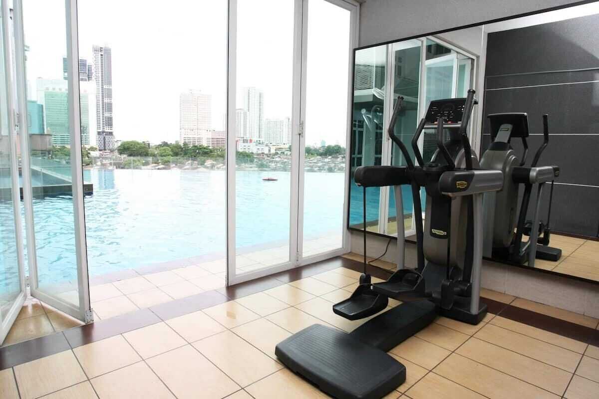 Un gimnasio con cinta de correr, elíptica y steper, con vistas a un cuerpo de agua y al paisaje urbano.
