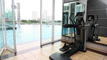 Un gimnasio con cinta de correr, elíptica y steper, con vistas a un cuerpo de agua y al paisaje urbano.