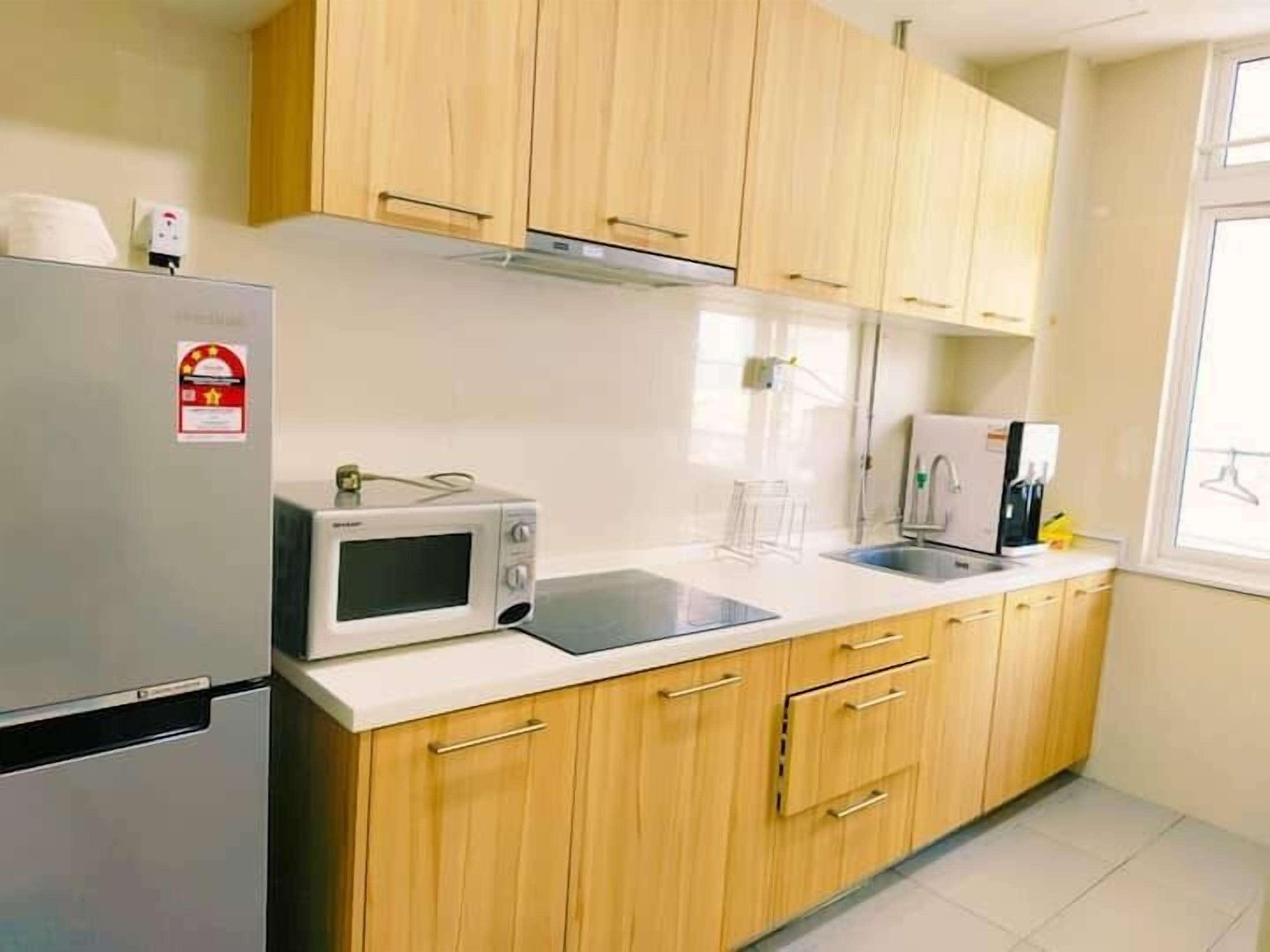 A kitchen with wooden cabinets, a stainless steel refrigerator, a microwave, a sink, and a window.