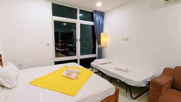 A hotel room with a bed, a massage table, a window with a view of the city at night, and a chair.