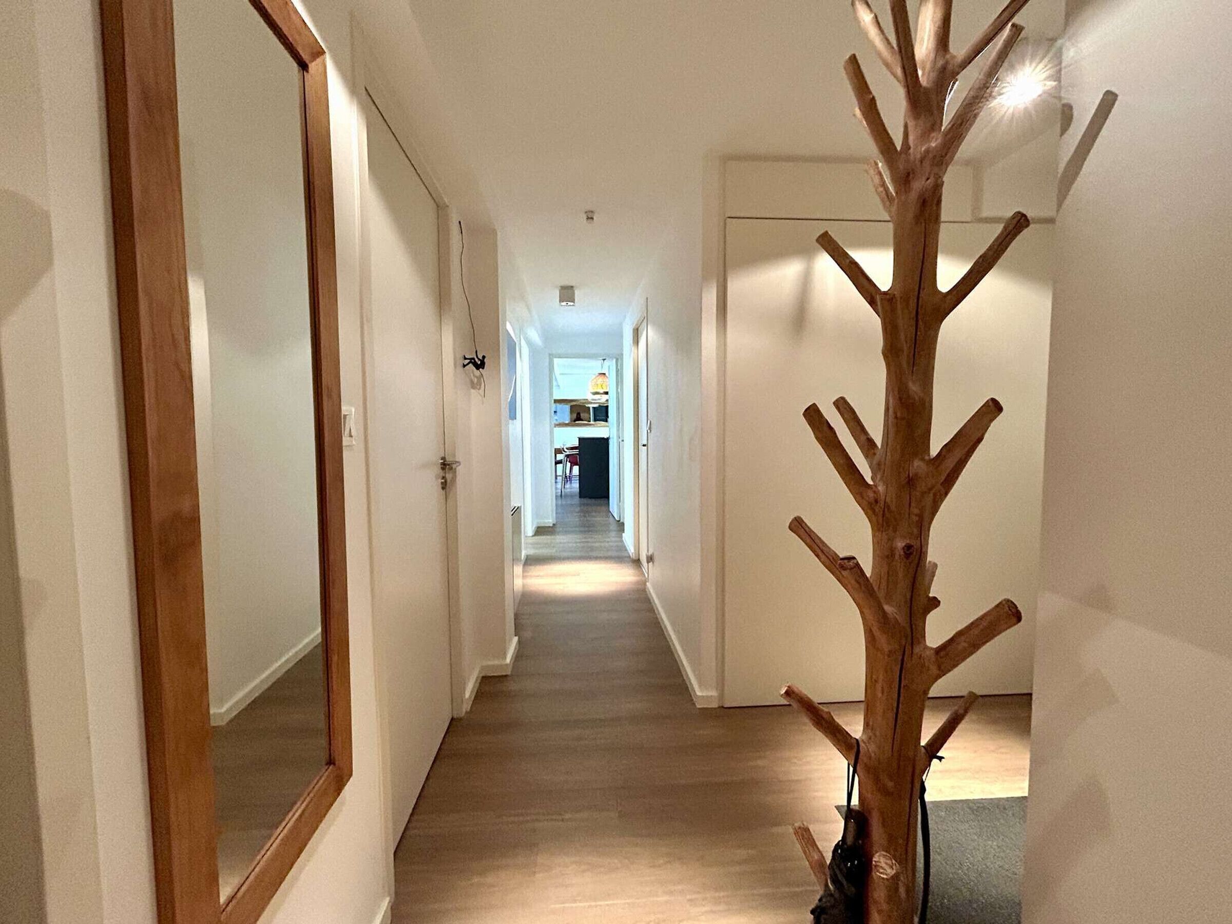 Un couloir étroit, doté d’un plancher en bois et de murs blancs, qui mène à un espace cuisine.