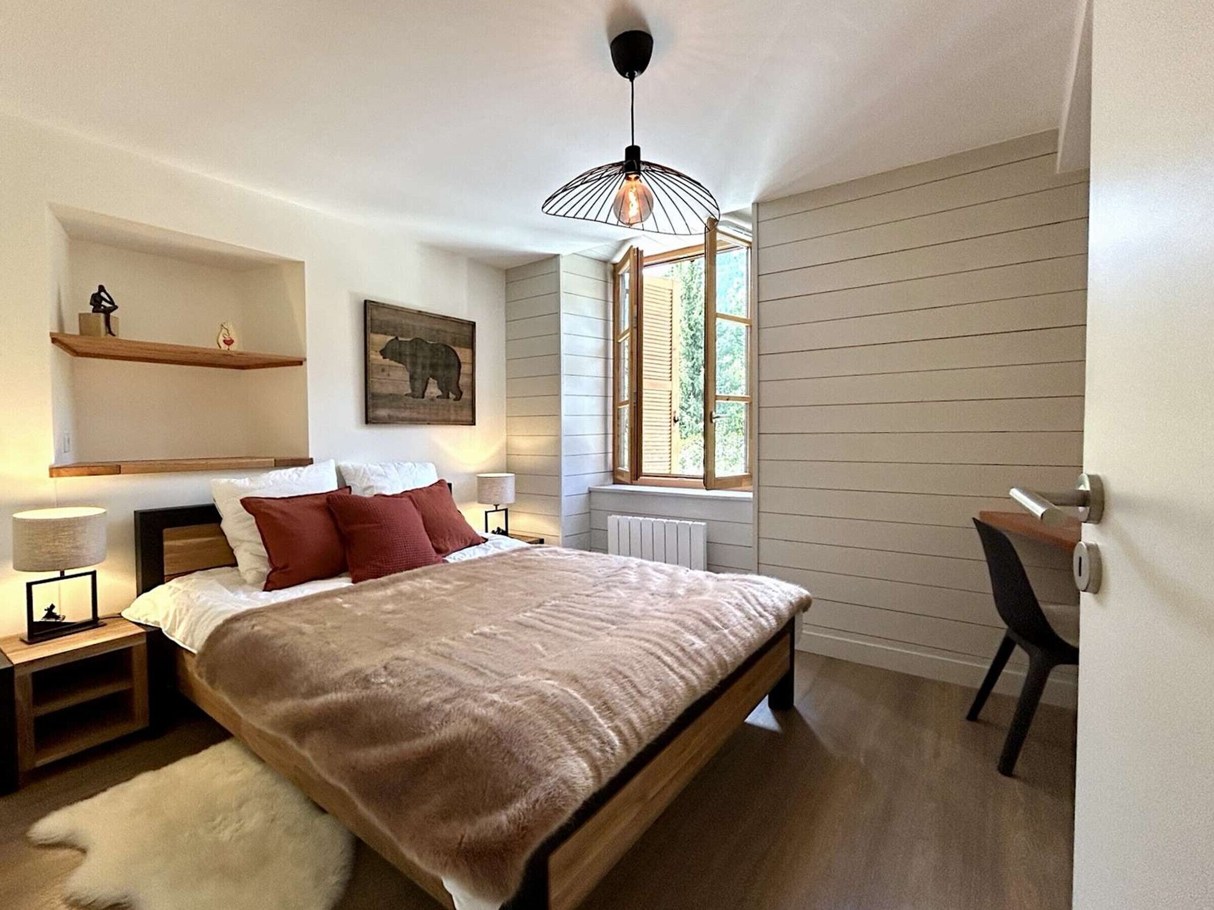Une chambre à coucher comprenant un lit, des tables de chevet, une chaise, une fenêtre et une étagère fixée au mur.