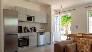 Una cocina moderna con electrodomésticos de acero inoxidable, un comedor con mesa y sillas de madera, y vistas a un árbol.