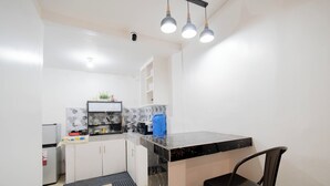 Een kleine keuken met witte kasten, een zwart aanrecht en een zwarte stoel.