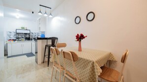 Een compacte keuken met witte kastjes, een aanrecht en een spoelbak. Er is een eethoek met een tafel bedekt met een tafelkleed met een patroon en twee houten stoelen.