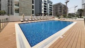 A swimming pool with lounge chairs and a view of a modern building under construction.