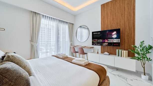 A modern hotel room with a large bed, a desk, a TV, and a potted plant.