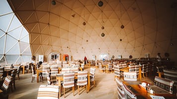 Un interior amplio con un techo alto y geométrico, y numerosas mesas y sillas dispuestas para comer.