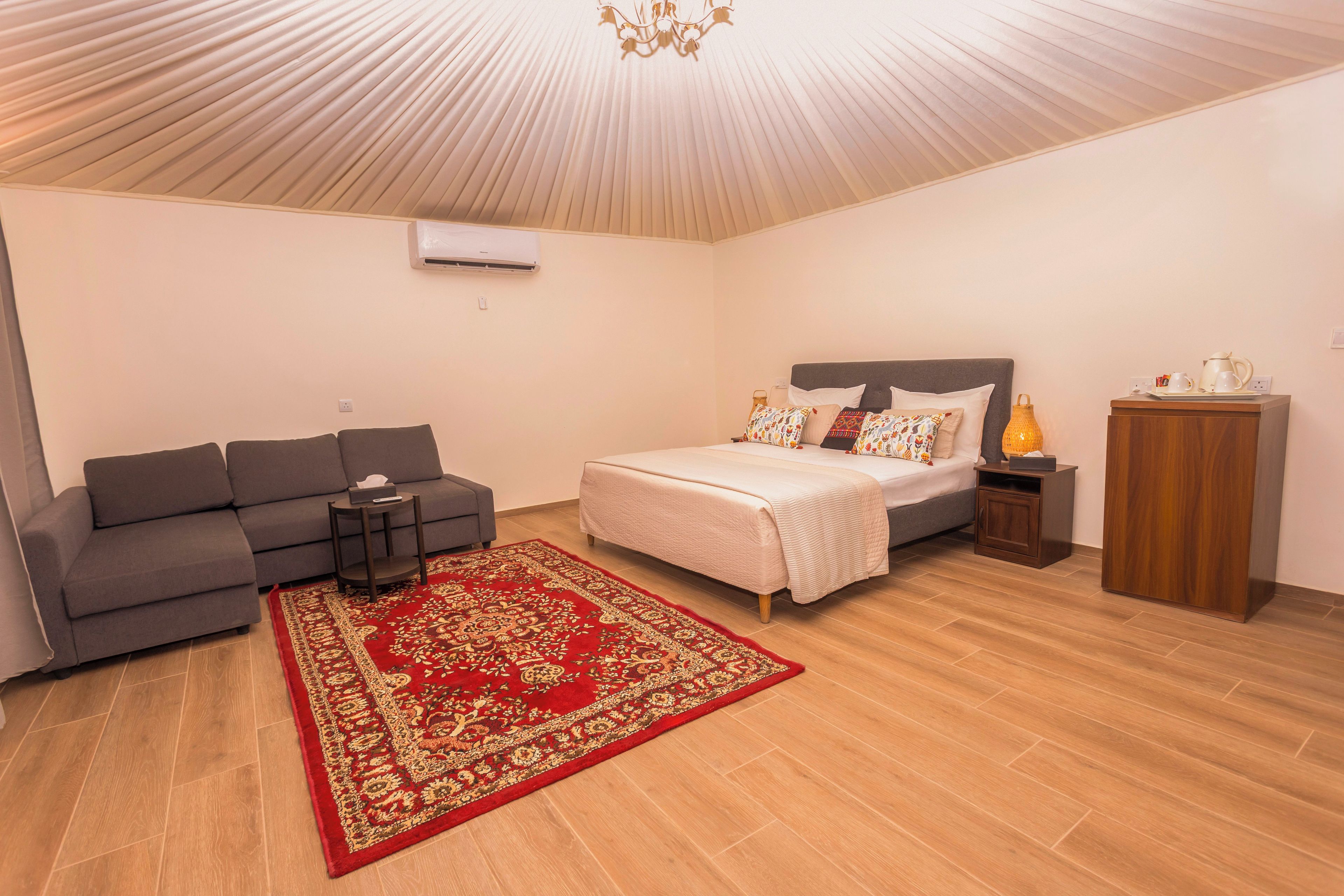 A bedroom with a bed, a sofa, a nightstand, a lamp, and a wooden cabinet.
