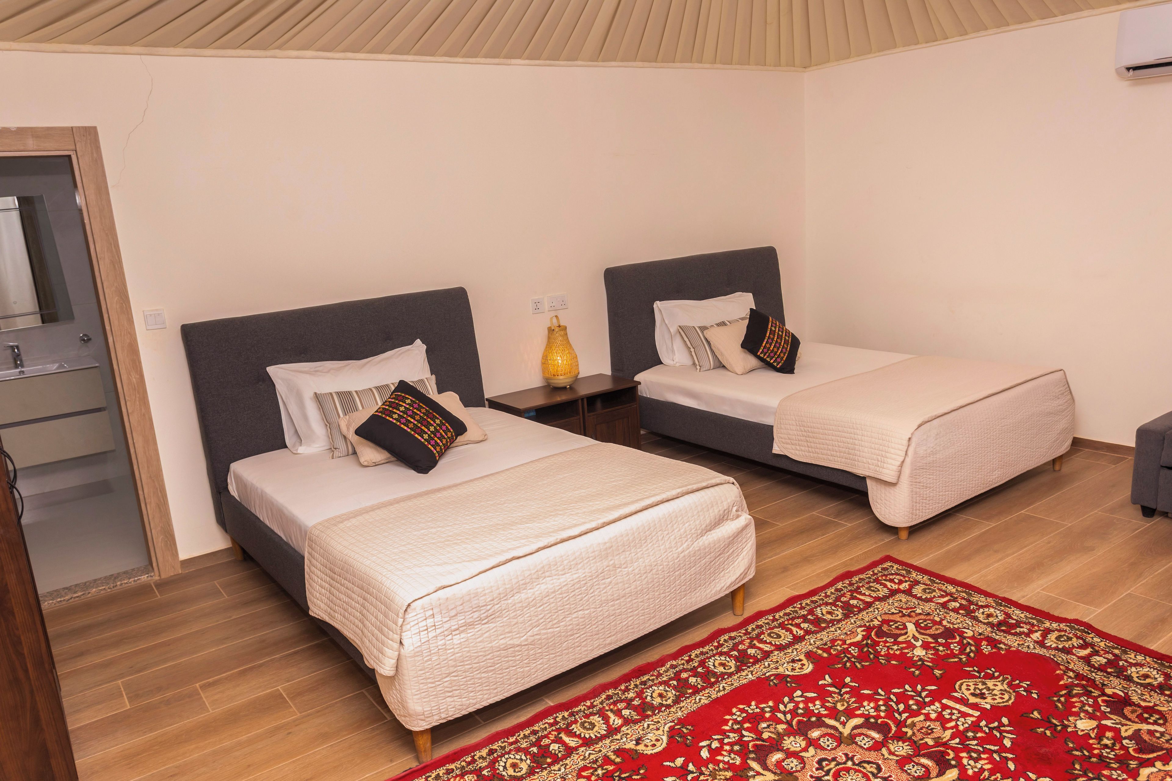 A hotel room with two beds, a wooden floor, and a red patterned rug.