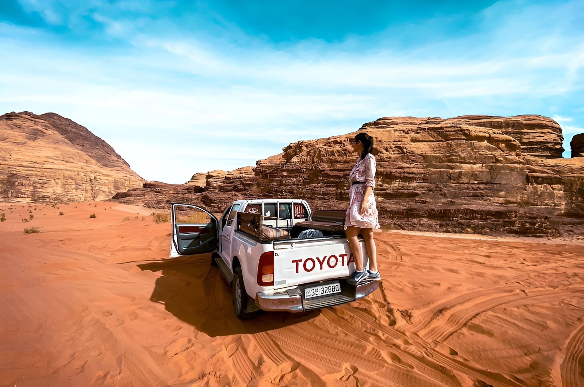 A desert landscape with a white Toyota pickup truck parked on a sandy area.