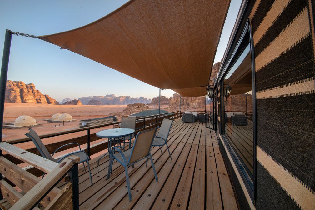 Une terrasse en bois avec des sièges d’extérieur, une grande voile d’ombrage et une vue sur les montagnes désertiques.