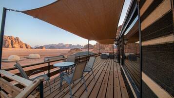 Une terrasse en bois avec des sièges d’extérieur, une grande voile d’ombrage et une vue sur les montagnes désertiques.