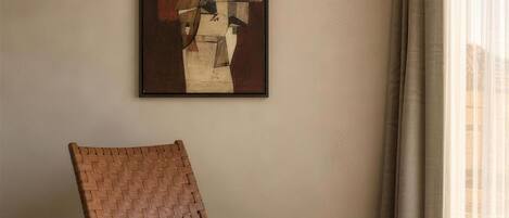A minimalist room with a modern chair, a colorful ottoman, and a geometric abstract painting on the wall.